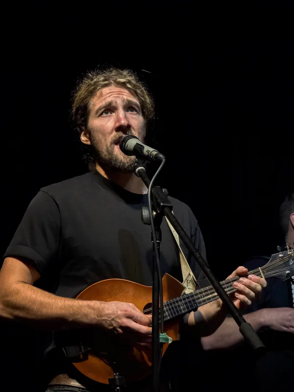 Ben Garrison singing into a microphone while playing mandolin
